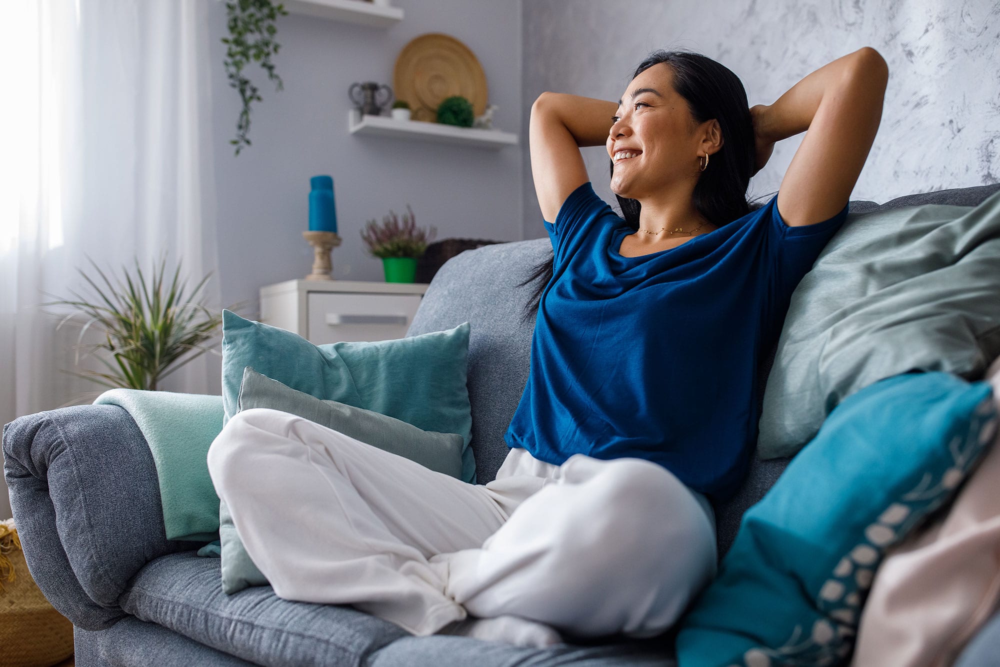 young woman lounging on sofa with hands behind head and daydreaming